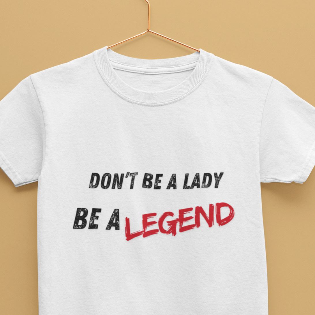 White crew neck t-shirt with the text 'DON'T BE A LADY BE A LEGEND' printed in red and black on a hanger against a beige background.