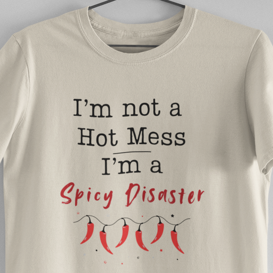 Beige t-shirt with text 'I'm not a Hot Mess, I'm a Spicy Disaster' on a hanger against a gray background
