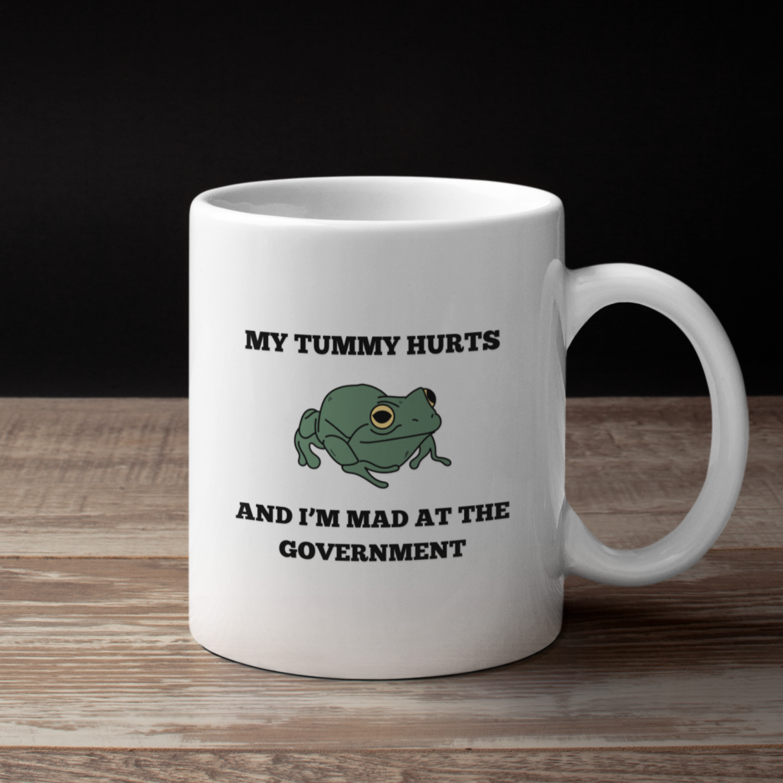 White mug with a frog graphic and text on a wooden surface with black background