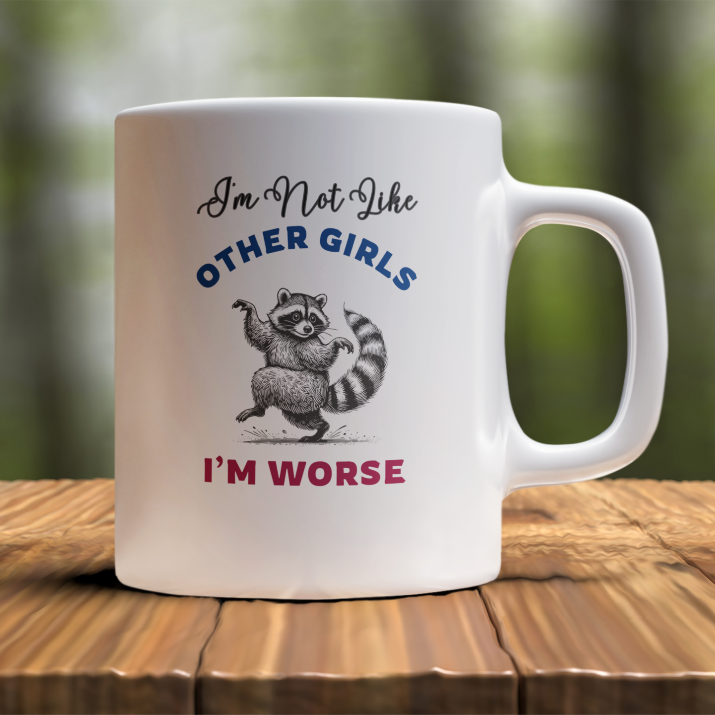 White mug with a raccoon graphic and text on a wooden surface with a blurred green background
